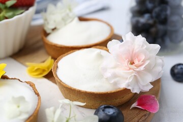 Delicious dessert. Tartlets with cream, berries and flowers on white tiled table, closeup