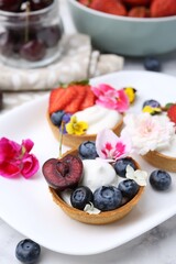 Sweet tartlets with berries and flowers on light marble table, closeup. Delicious dessert