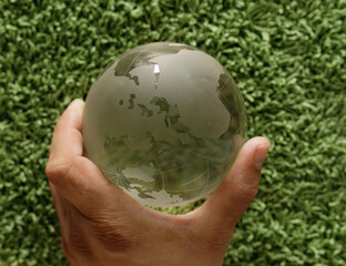A hand gently holds a frosted glass globe, resting on a lush green carpet.  Global concepts,...