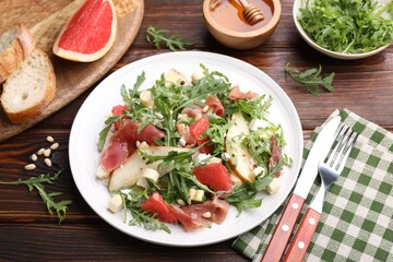 Tasty salad with arugula, prosciutto, cheese, pear, grapefruit and nuts on wooden table, above view