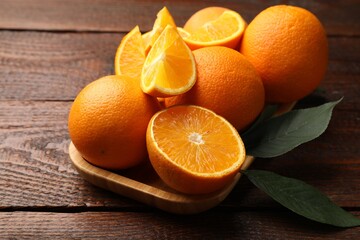 Fresh ripe oranges and leaves on wooden table, closeup