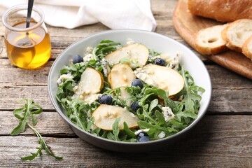 Tasty salad with arugula, pear, blue cheese, peanuts and blueberries in bowl on wooden table, closeup