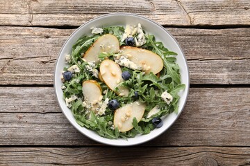 Tasty salad with arugula, pear, blue cheese, peanuts and blueberries in bowl on wooden table, top view