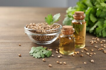 Aromatic oil in bottles, cilantro leaves and coriander seeds on wooden table, closeup