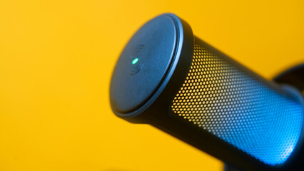 Modern professional USB podcast microphone with glowing LED light set against a vibrant yellow background, ideal for streaming and audio recording setups. Photo