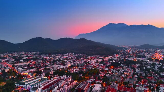 City lights switched on in the cityscape of resort Kemer, Turkey. Drone footage over the scenery at sunset. Pink sky among the rocks silhouettes at backdrop.