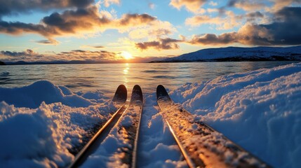Two cross-country skis lying on the snow, with a sunset in the background
