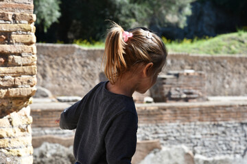 little girl exploring ancient ruins during a sunny day outdoors. She appears curious and immersed...