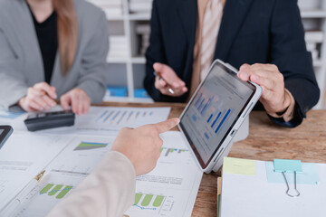 Business colleagues are discussing company performance and analyzing financial data displayed on a digital tablet and paper charts during a productive office meeting