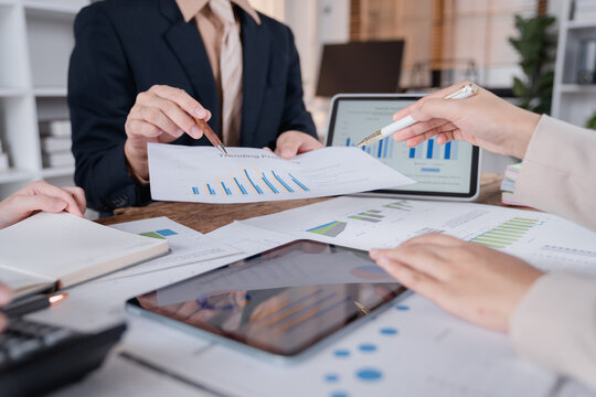 Business team analyzing financial charts and graphs using digital tablet and documents during a meeting, discussing company performance and planning future strategies