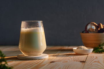 Creamy adaptogenic mushroom latte in a clear glass stands on a wooden table in warm morning light,...
