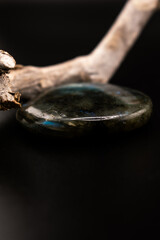 blue-green labradorite stone rests beside textured driftwood on a dark background. The contrast of...