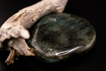 blue-green labradorite stone rests beside textured driftwood on a dark background. The contrast of glossy crystal and rustic wood creates a serene, natural composition for wellness or decor themes.