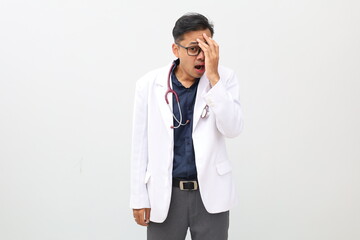 Asian male doctor wearing a doctor's coat and stethoscope, peeks out in shock while covering his...