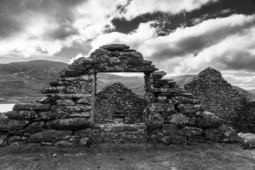 Black and white image of a ruined stone wall with window opening, framing distant mountain scenery...
