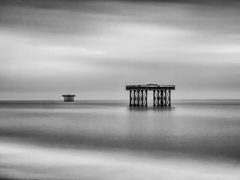 Black and white long exposure of abandoned cooling platforms on stilts off the coast at Sizewell, isolated in tranquil sea under soft sky