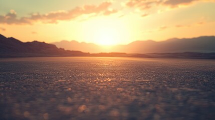 Obraz premium A vast, empty desert landscape with a setting sun casting a warm glow over the horizon. The sky is a gradient of orange and yellow hues