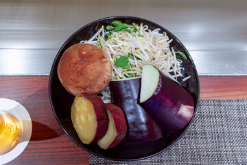 Fresh teppanyaki vegetables including eggplant, sweet potato, shiitake, and sprouts arranged in a bowl on a wooden table