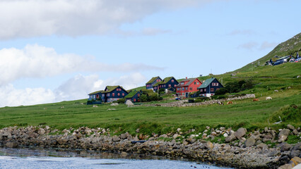 A picturesque coastal village in the Faroe Islands features vibrant houses nestled against a lush...