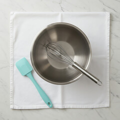 Overhead view of a mixing bowl with a whisk and spatula on a white cloth.