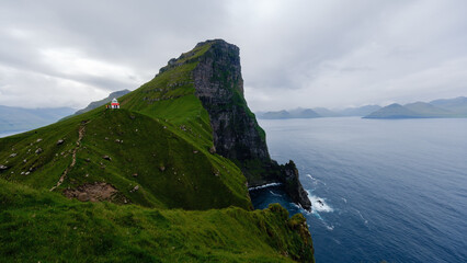 Rugged cliffs rise dramatically above the Atlantic Ocean in the Faroe Islands. Lush green slopes...