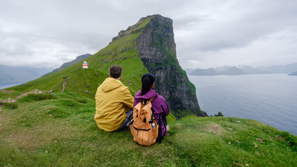 Two hikers relax on a grassy hillside, admiring the stunning landscape of Slaettaratindur in the...