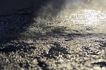 Close-up of wet stone surface steaming in direct sunlight, water droplets evaporating, sharp shadows and glare