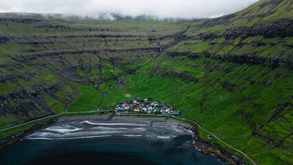 A tranquil village rests within lush green hills of the Faroe Islands, surrounded by steep cliffs...
