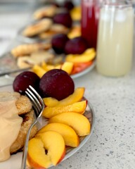 Top view of a light summer breakfast. Plates with homemade cottage cheese pancakes topped with condensed milk, fresh sliced nectarines, and whole plums. Refreshing fruit juice with ice