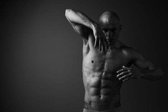 Strong man posing gracefully in black and white photography, showcasing his muscular physique and dynamic movement, capturing the essence of strength and artistry.
