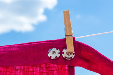 Magenta linen skirt snap button details hanging on clothesline under bright cloudy sky