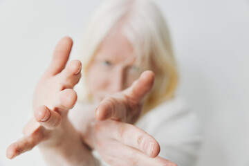 White haired person reaching out with hands against a plain background, conveying a sense of...