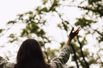 Woman embracing nature in forest back view with arms raised. A girl enjoying the peace, harmony and...