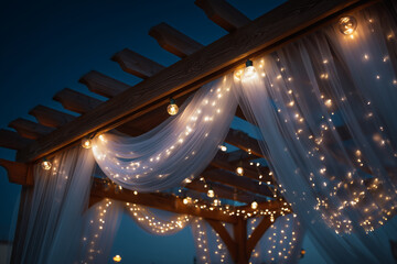Wooden pergola draped with sheer white fabric and illuminated by warm string lights at dusk wooden structure