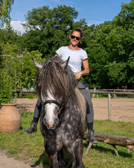 Woman enjoying ride on dapple gray horse along rural dirt road, surrounded by open farmland....