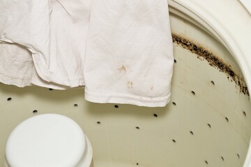 Broken dirty washing machine drum oil and grease stains white stained shirt.	