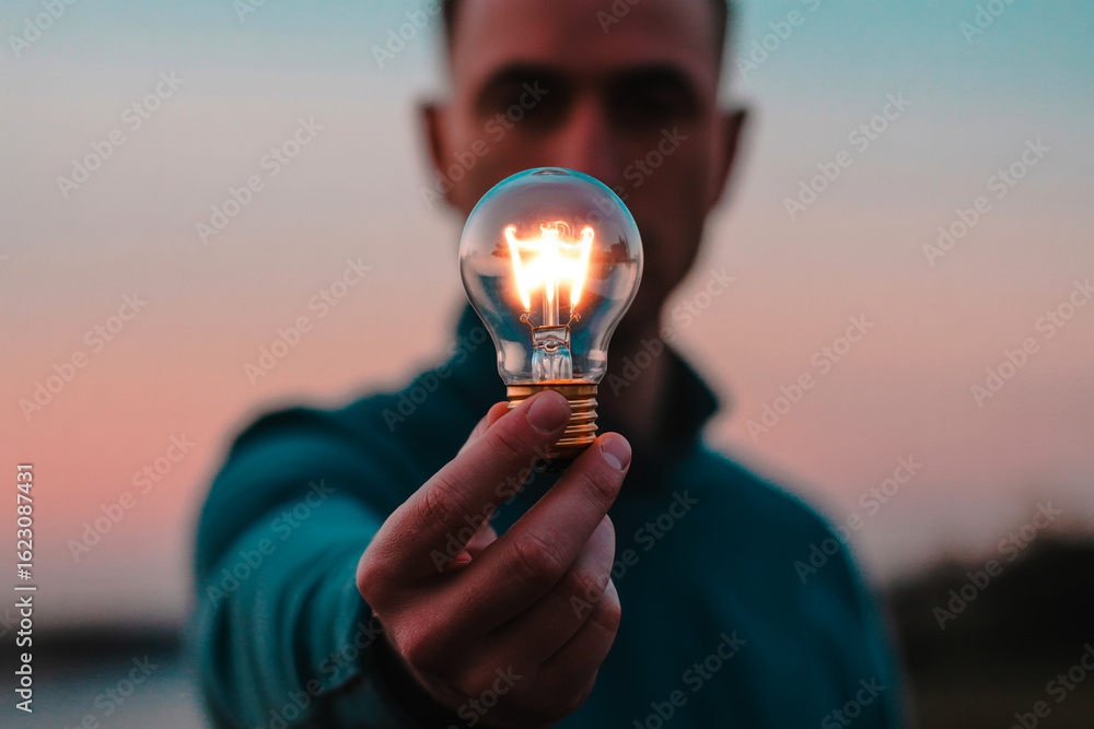 Poster man holding glowing light bulb displaying innovation and creative thinking on evening sky background