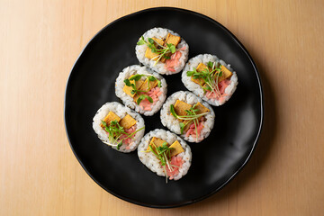 Overhead shot of six delicious tamagoyaki sushi rolls, garnished with microgreens and pickled ginger, arranged on a black plate.  Food photography.