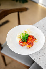 Appetizing chicken with melted cheese and red sauce served with mashed potatoes garnished with green onions and parsley on a white plate, close-up shot.