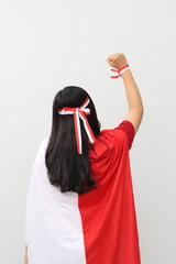 Back view of Indonesian woman with red and white ribbon standing while clenching fist to celebrate...