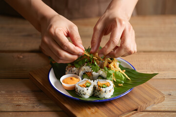 Chef's Hands Garnish Exquisite Asian Fusion Food: Crispy Tempura, Cilantro, and Spicy Mayo Sushi Rolls.