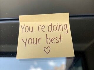 A yellow sticky note with the message "You're doing your best" written in brown ink, offering encouragement and positivity.