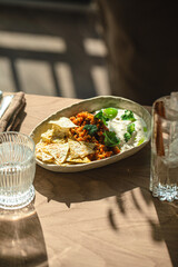 Bowl with cream dip, minced topping and crispy tortilla chips on table