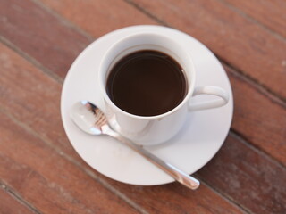 A hot, dark espresso in a white ceramic mug sits on a wooden table, its rich aroma promising a morning break