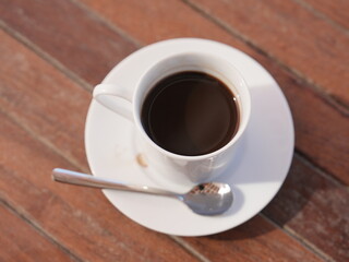 A hot, dark espresso in a white ceramic mug sits on a wooden table, its rich aroma promising a morning break