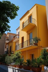 Fototapeta premium Vibrant yellow building with balconies and plants on a sunny day