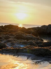 Title: Orange sunlight reflects off the calm ocean as the sun sets over the horizon, painting the sky with beautiful clouds