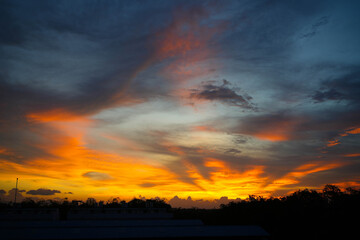 Title: Orange sunlight reflects off the calm ocean as the sun sets over the horizon, painting the sky with beautiful clouds