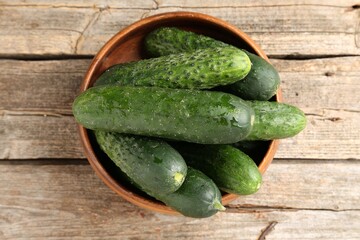 Fresh cucumbers in bowl on wooden table, top view