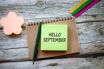 HELLO SEPTEMBER written on a sticky note on a brown notebook. isolated on a beautiful wooden table.